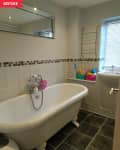 Clawfoot bathtub in a tiled bathroom with a mirror, towel rack, and colorful bath toys by the window.