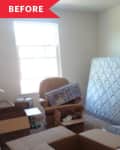 Cluttered room with a mattress against the wall, boxes, an armchair, and a window.