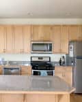 Spacious kitchen with light wood cabinets, granite countertops, stainless steel appliances, and a red rice cooker.