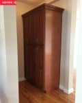 Tall wooden cabinet with six doors in a narrow hallway, hardwood floor.