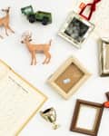 Open book with cursive writing, toy deer, green toy car, empty frames, and a small trophy on a white surface.