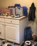 Cluttered mudroom with white cabinets, shoes, bags, and assorted items on the counter and floor.