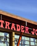 Trader Joe's storefront with red signage and wooden beams under a clear blue sky.