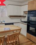 Wooden kitchen with white cabinets, double oven, gas stove, and island with chairs.