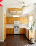 Bright kitchen with oak cabinets, white appliances, dark wood floor, and a potted plant by sliding glass doors.