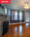 Empty living room with blue walls, wooden floor, stone fireplace, ceiling fan, and small wooden table by the door.