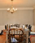 Dining room with wooden table, mismatched chairs, chandelier, striped wallpaper, and moving boxes.