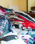 Cluttered bed with piles of clothes, hangers, and a "Before" label in a bedroom.