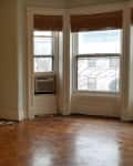 Empty living room with a decorative fireplace, parquet floor, and three large windows with bamboo blinds.