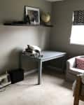 Home office with gray desk, sewing machine, wall shelf, globe, and framed photo. Mirror and armchair with red chevron pillow.
