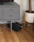 Gray mid-century modern console with TV, gaming console, and tangled cables on wooden floor.