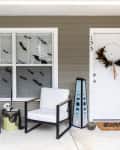 Porch featuring Halloween DIYs, including a skeleton topiary, bats on the window, a spooky luminary, painted doormat, and feathered wreath