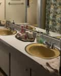 Before: Dated bathroom with beige walls, cornflower sinks, and white vanity