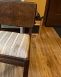 Wooden chair with striped cushion on wooden floor, next to a vintage green dresser.