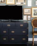 Before: TV on top of a black dresser, against a gallery wall filled with gold-framed artwork