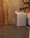 Before: Laundry area in unfinished basement with wood paneling and wires overhead