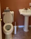 Before: Half bathroom with dark orange walls, white pedestal sink, and beige floors