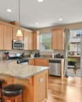 Spacious kitchen with light wood cabinets, granite island, bar stools, stainless steel appliances, and sliding glass doors.