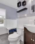 Small bathroom with white wainscoting, dark wood vanity, and wall shelves above toilet.