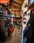 Cluttered garage with tools on pegboard, shelves with paint cans, and various storage boxes.