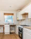 Small kitchen with white cabinets, wood countertops, gas stove, and a window with a wooden blind.