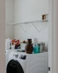 Laundry room with washer, dryer, cleaning supplies, wicker vase, and teal watering can on top.