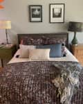 Bedroom with a patterned bedspread, two side tables, lamps, and framed photos on the wall.