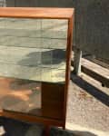 Wooden display cabinet with glass shelves and sliding doors, placed outdoors on a concrete surface.
