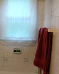 Bathroom with floral tile, red towel, and sheer curtain over window.
