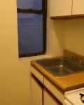 Small kitchen with a single window, wooden countertop, stainless steel sink, and a white gas stove.