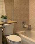 Small bathroom with beige tiles, white sink, toilet, bathtub, and potted plant on the counter.
