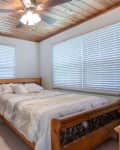 Bedroom with wooden bed frame, nightstand, ceiling fan, and blinds on windows.