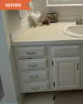 Bathroom vanity with white cabinets, single sink, and countertop items including a glass jar, framed photos, and toiletries.