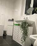 Bathroom with black tile floor, white sink, hanging plant, shower, and textured cabinets.
