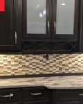 Dark wood kitchen cabinets with frosted glass doors, checkered tile backsplash, and a marbled countertop.