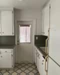 Small kitchen with white cabinets, gray countertops, and a patterned floor, featuring a door with a window.