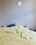 Unmade bed with yellow sheet, black water bottle, and orange lamp on bedside table.