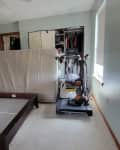 Disorganized bedroom with a bed frame, mattress leaning against wall, treadmill, and open closet.