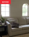 Beige sofa with studded trim, brown and patterned pillows, next to a wooden side table with a potted plant.