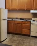 Kitchen and entry area of studio apartment. No furnishings, dated wood cabinets