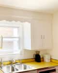 White kitchen cabinets before makeover with metal pulls. Yellow countertop and white trim, window, sink