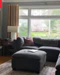 living/family room before makeover. Dark gray sectional, beige curtains, large window, gray walls with white trim