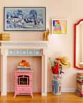 After: A pink fireplace surround with a pink electric fireplace in the hearth, set against a pink living room wall. There is art on either side of the faux fireplace, and a Frame TV hung above it with a blue and white landscape on display.