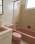 White painted vintage bathroom with pink sink, toilet, and bathtub before renovation. Neutral colored tiles line sink and tub.