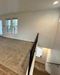 And empty room at the top of the stairs with white walls and beige carpet