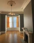wood floors, dark green walls, white molding. ornate molding around chandelier, fireplace, orange curtains