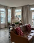 A living room with five large windows ceiling to floor curtains.