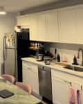 An apartment kitchen with white cabinets next to a dining table with pink chairs.