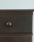 A brown three drawer night stand in a bedroom.