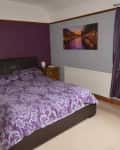 Neatly made bed in bedroom with purple accent wall before remodel.
